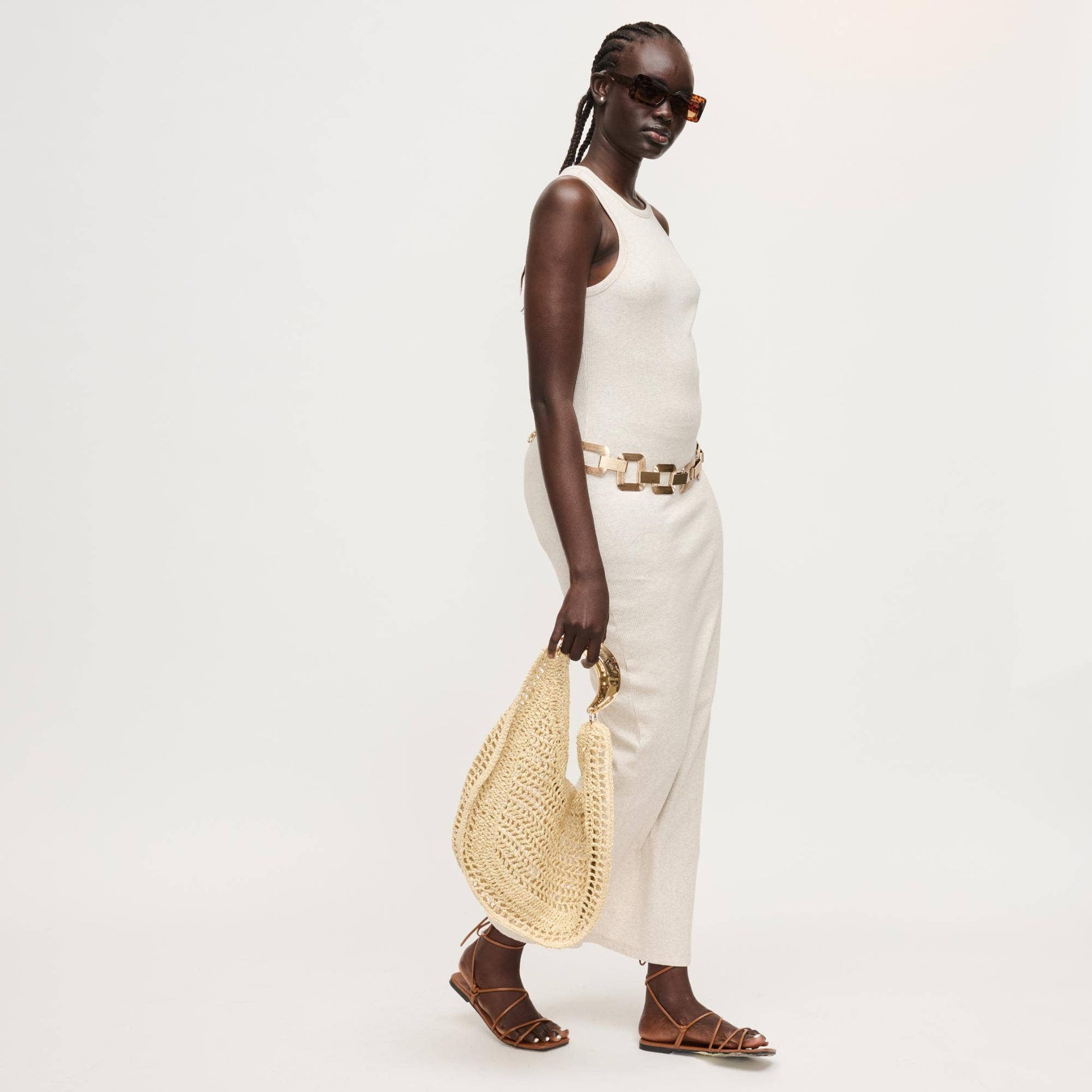 Woman in white outfit holding a straw bag on a plain background