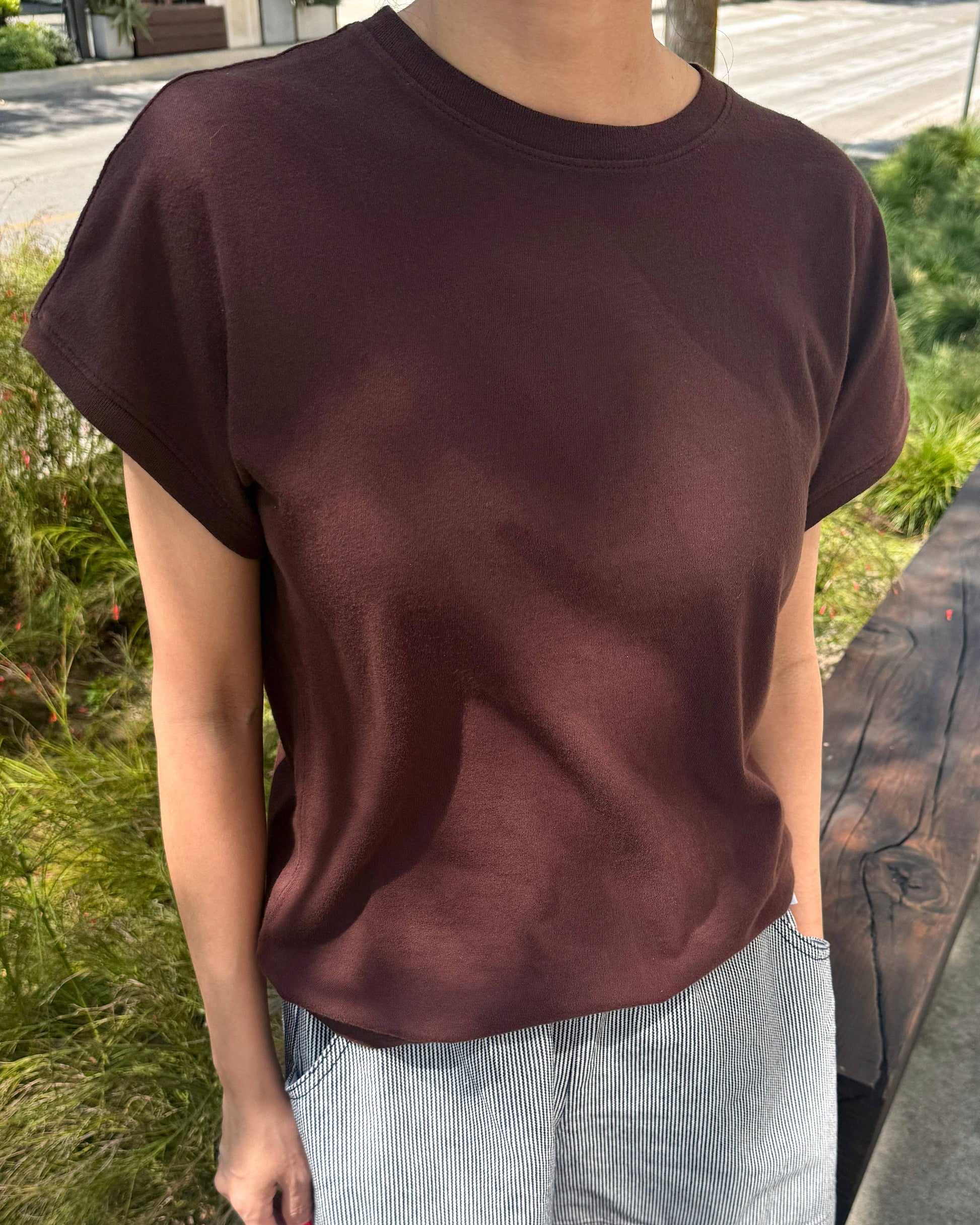 Person wearing a brown t-shirt and light gray shorts standing outdoors.