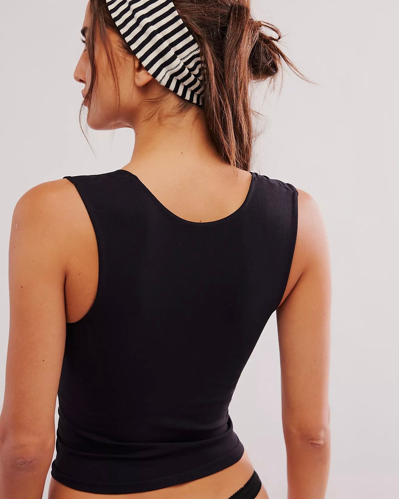 Back view of a model standing wearing the Free People Clean Lines Muscle Cami tank top in front of a white wall. 