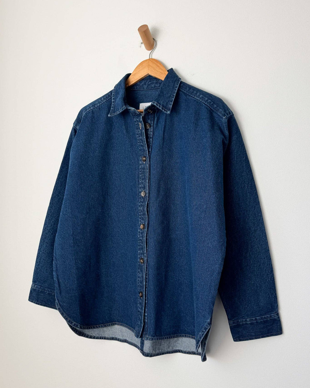 Blue denim shirt on a wooden hanger against a white background