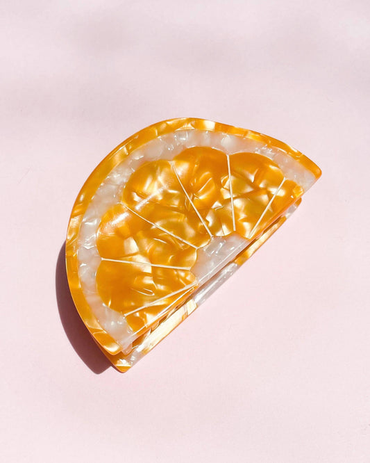 Orange slice shaped hair clip on a pink background