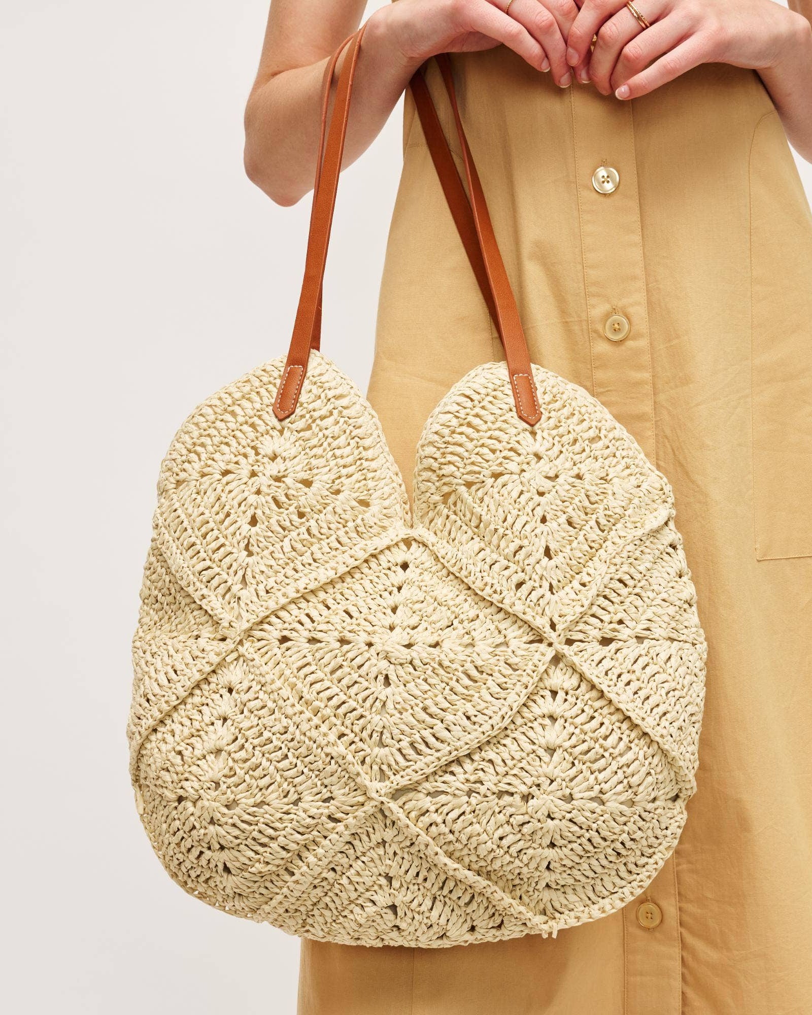 Beige woven handbag held by a person wearing a beige dress on a light background