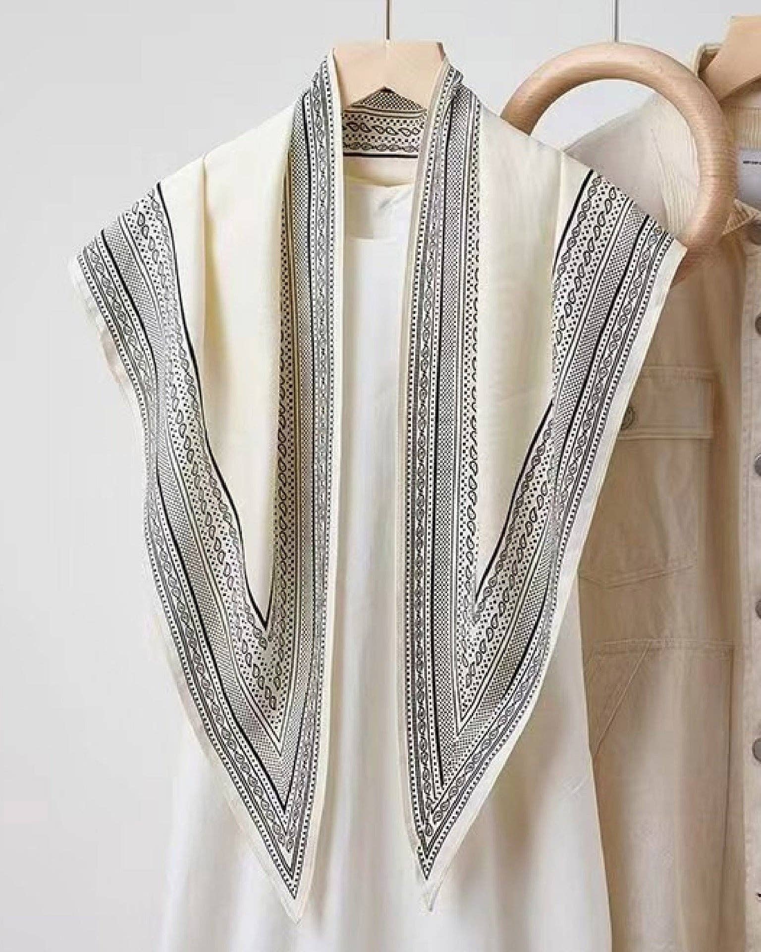 White shirt with black embroidery on a wooden hanger against a white background
