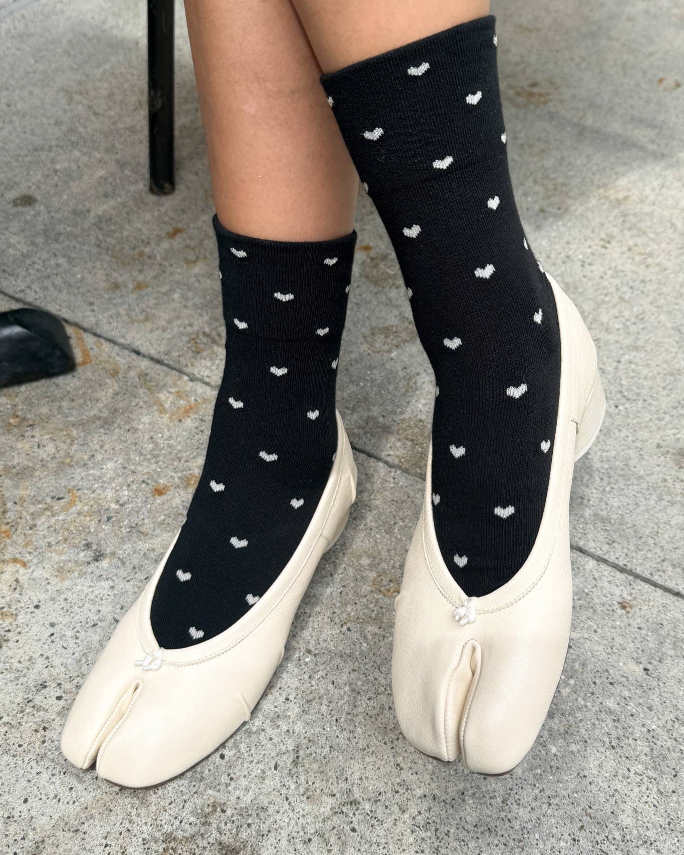 Person wearing black socks with white patterns and white shoes on a gray pavement.