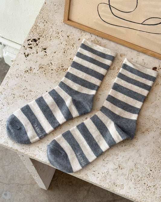 Pair of gray and white striped socks on a stone surface with abstract art in the background.