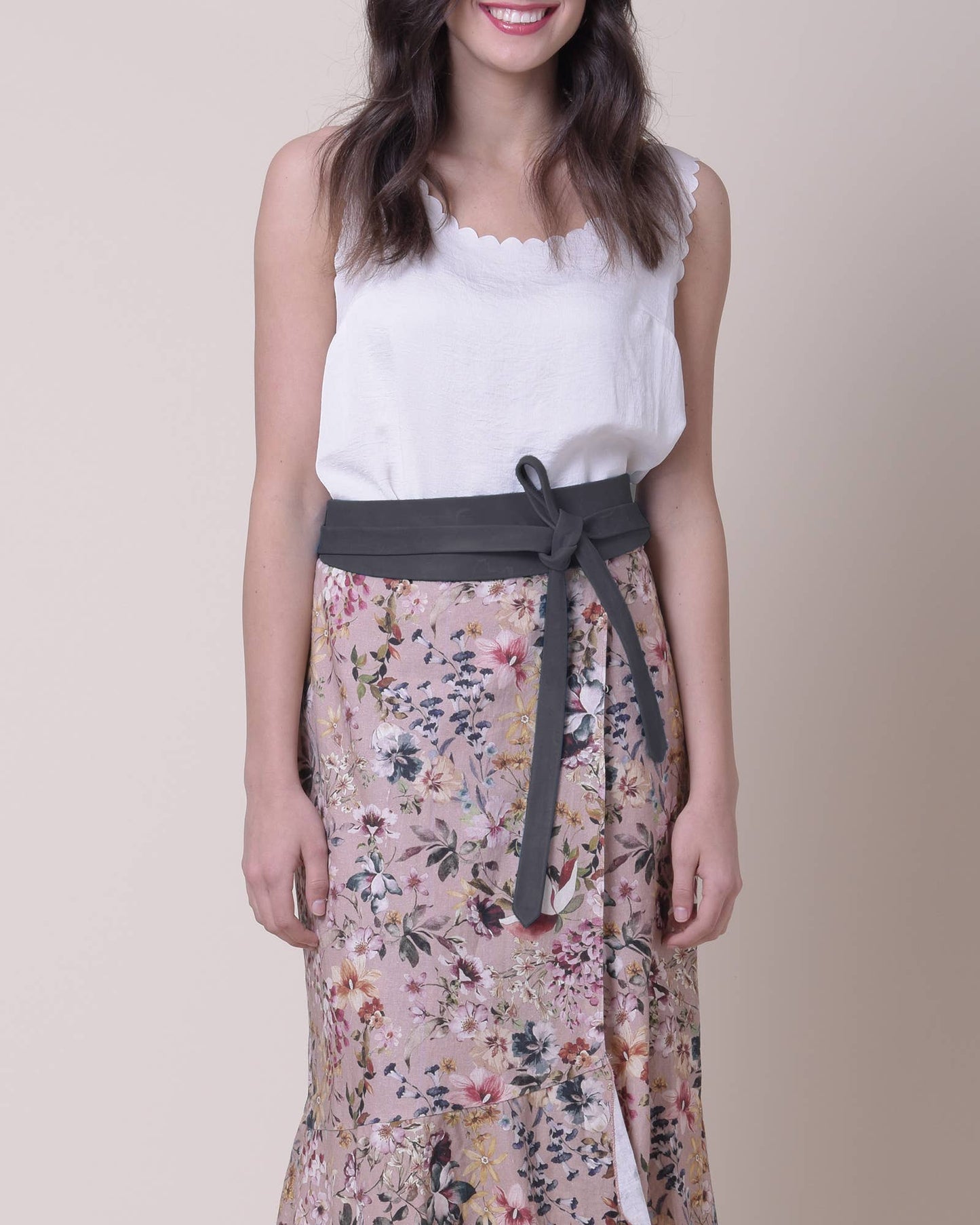 Woman wearing a white top and floral skirt with a gray belt on a beige background