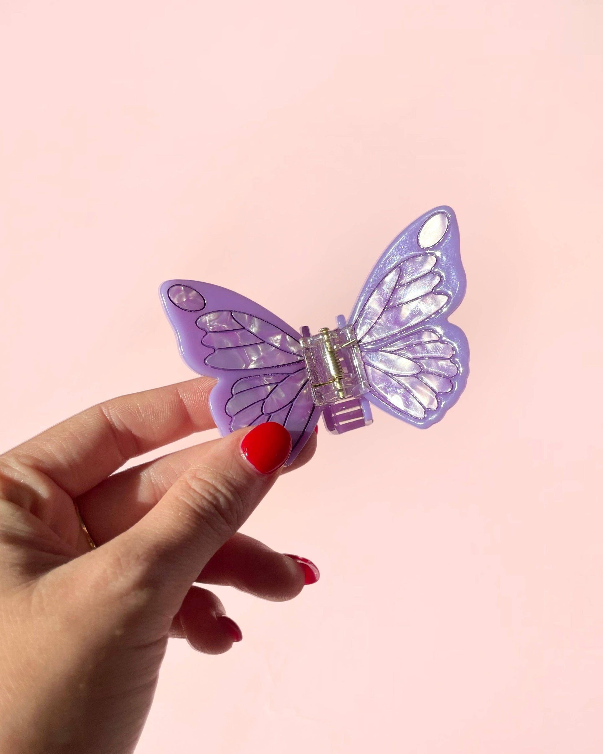 Hand holding a purple butterfly-shaped hair clip against a pink background