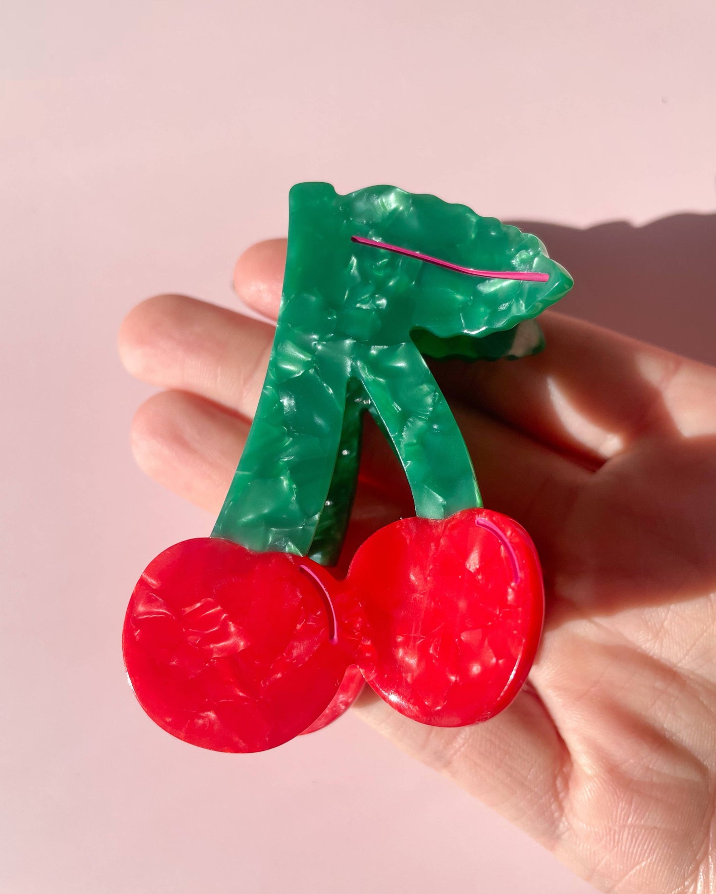 Hand holding a cherry shaped hair clip on a pink background