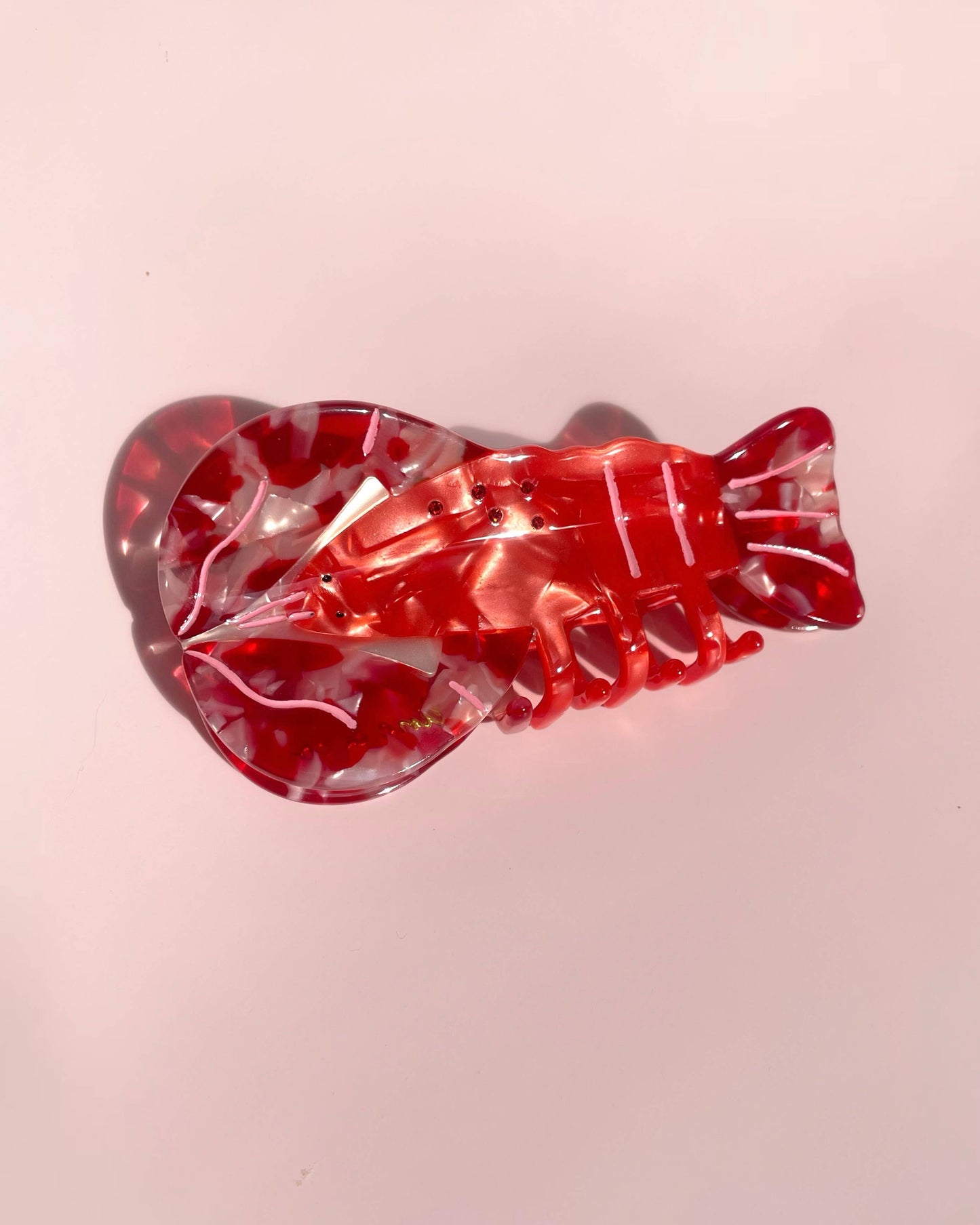Red and clear lobster-shaped hair clip on a pink background