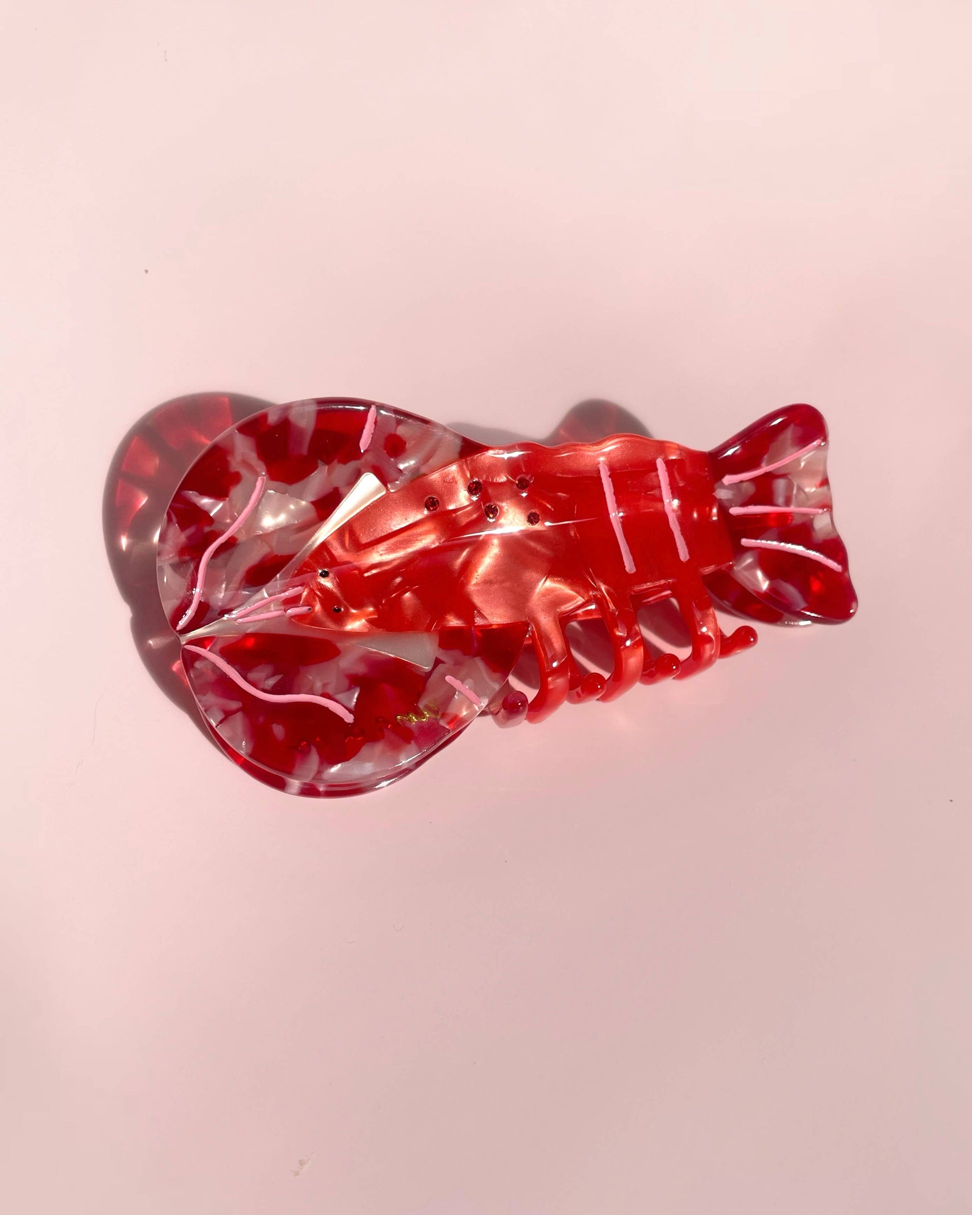Red and clear lobster-shaped hair clip on a pink background