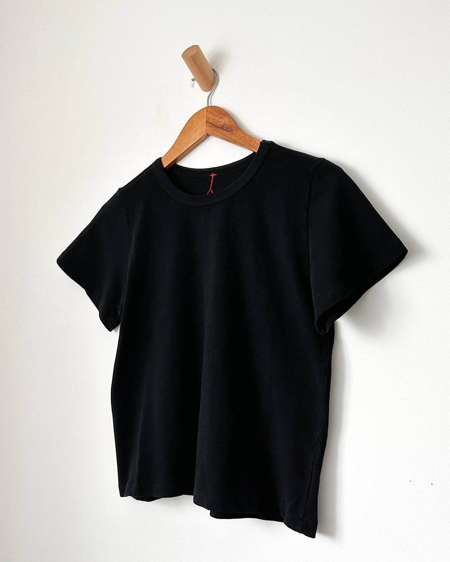 Black t-shirt on a wooden hanger against a white background