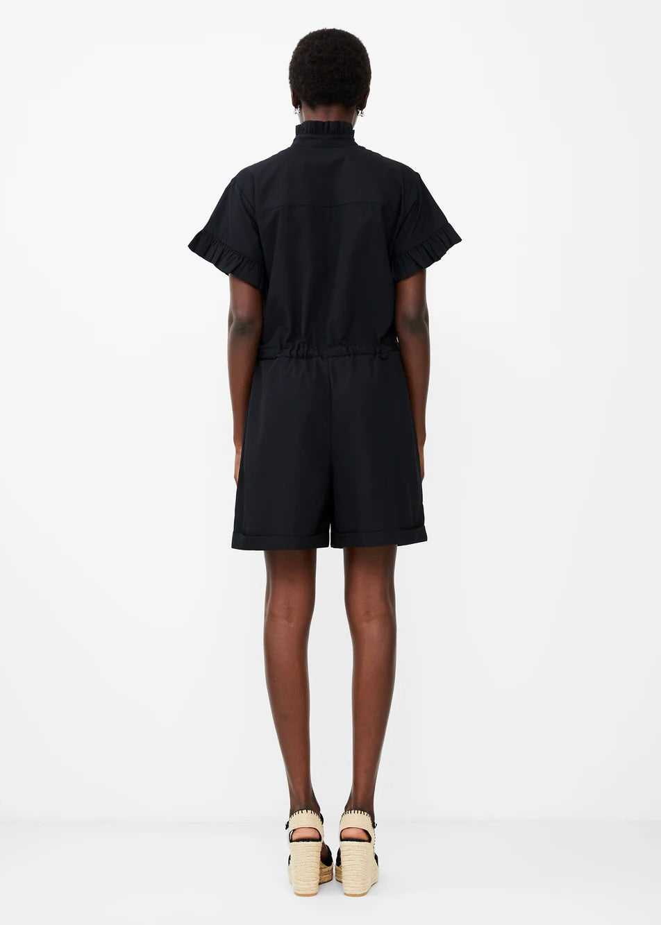 Back view of model wearing French Connection Eva Poplin Playsuit in black with hands at their side against a white background.