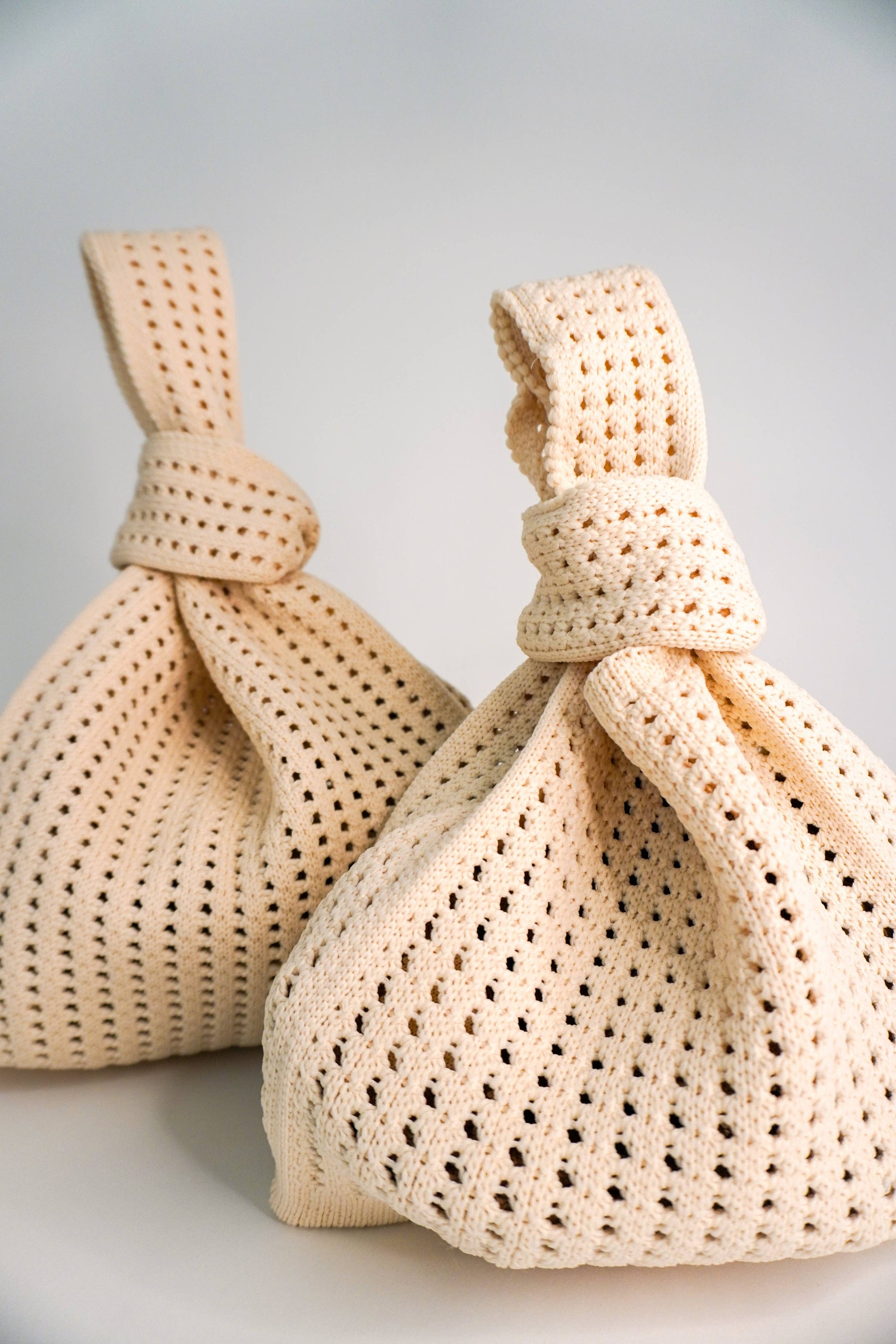 Two beige woven bags tied with strings on a light gray background