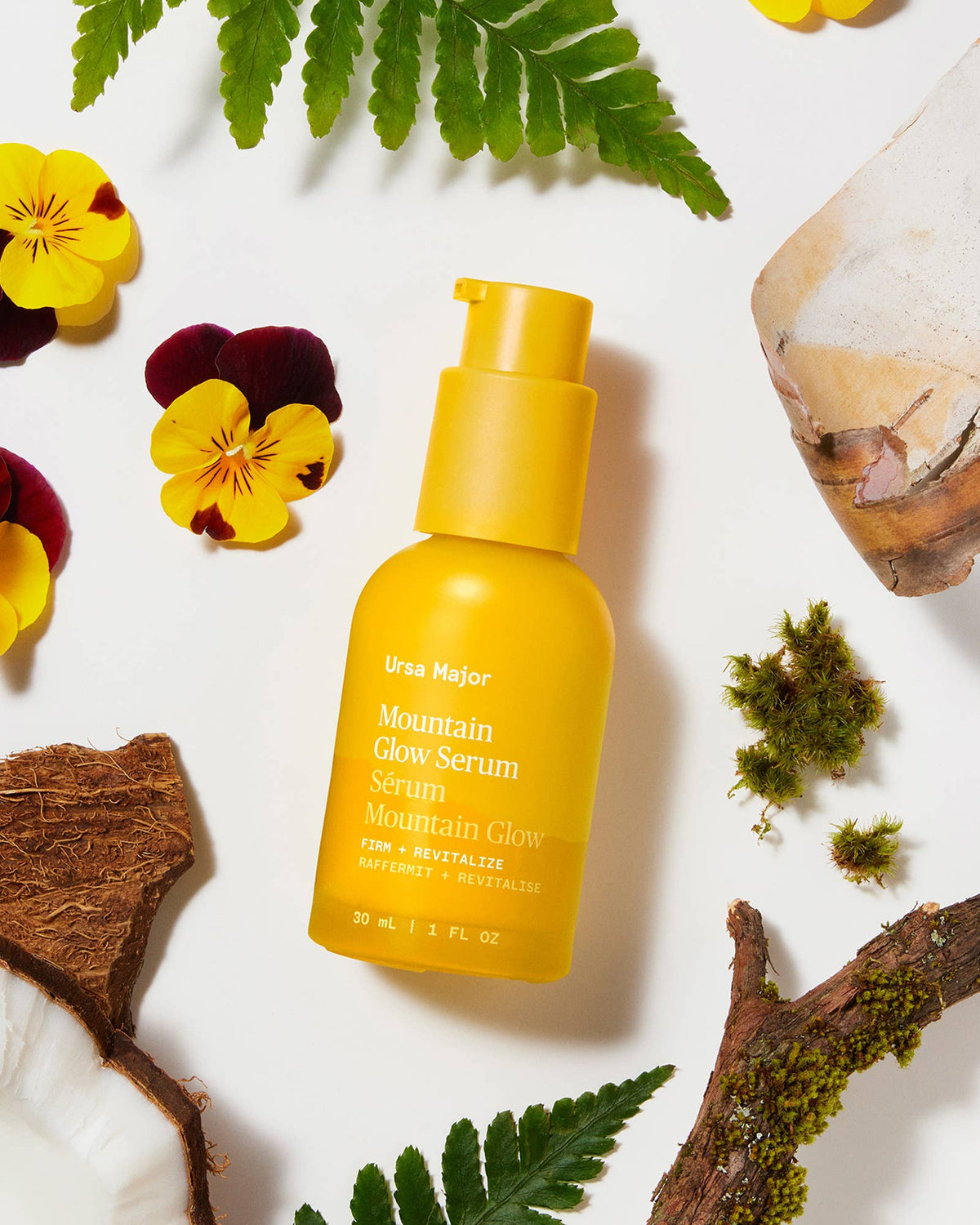 Yellow serum bottle labeled 'Ursa Major Mountain Glow Serum' surrounded by natural elements on a white background