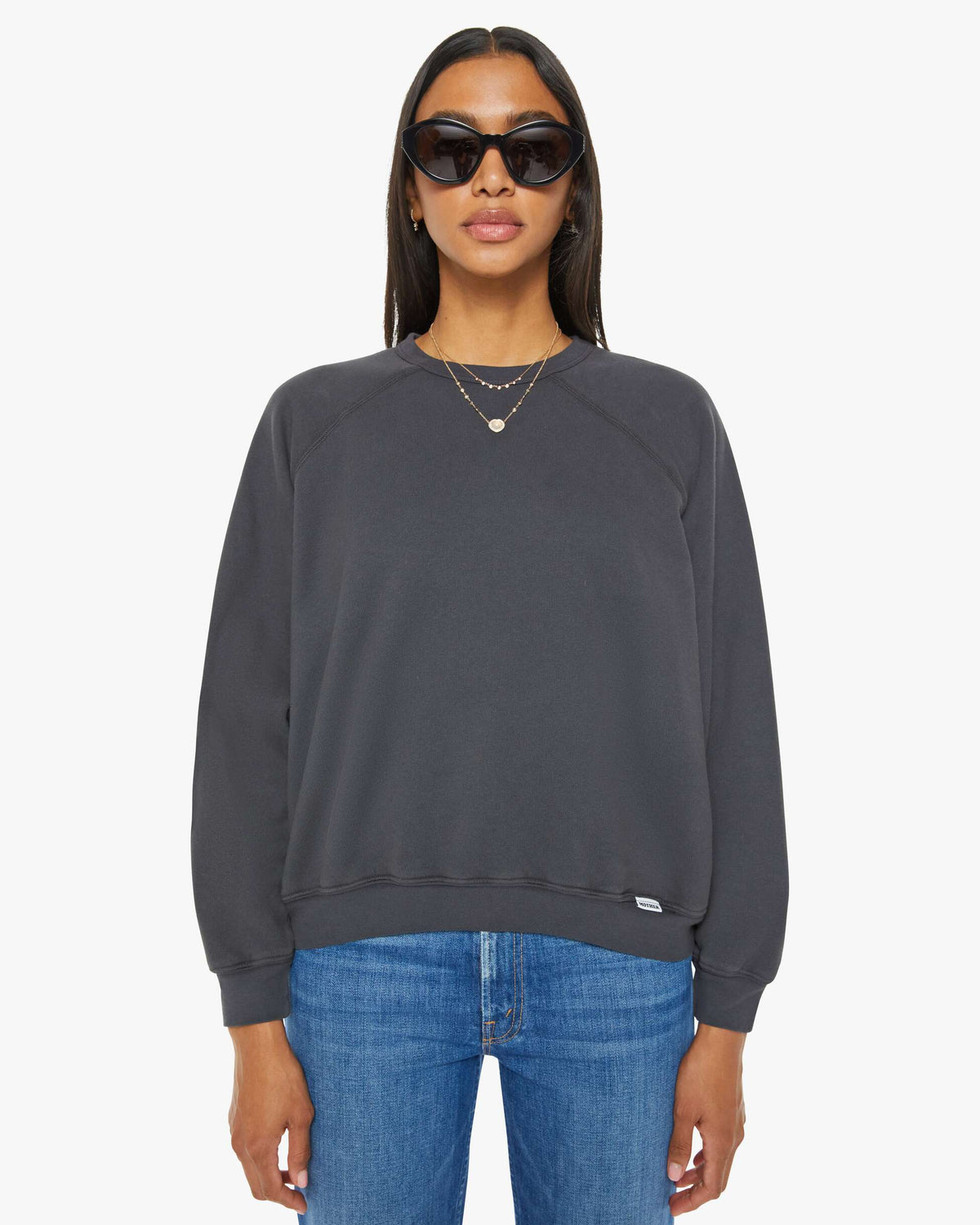 Woman wearing a dark gray sweatshirt and blue jeans on a white background