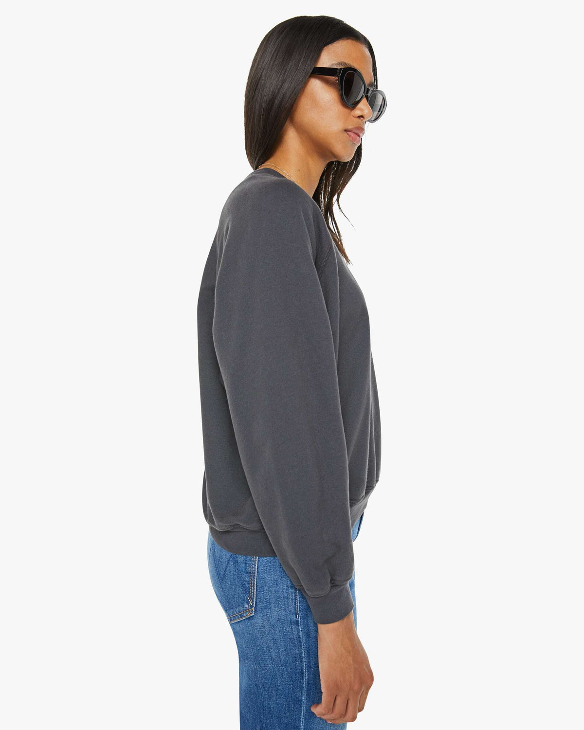 Woman wearing a dark gray sweatshirt and blue jeans on a white background