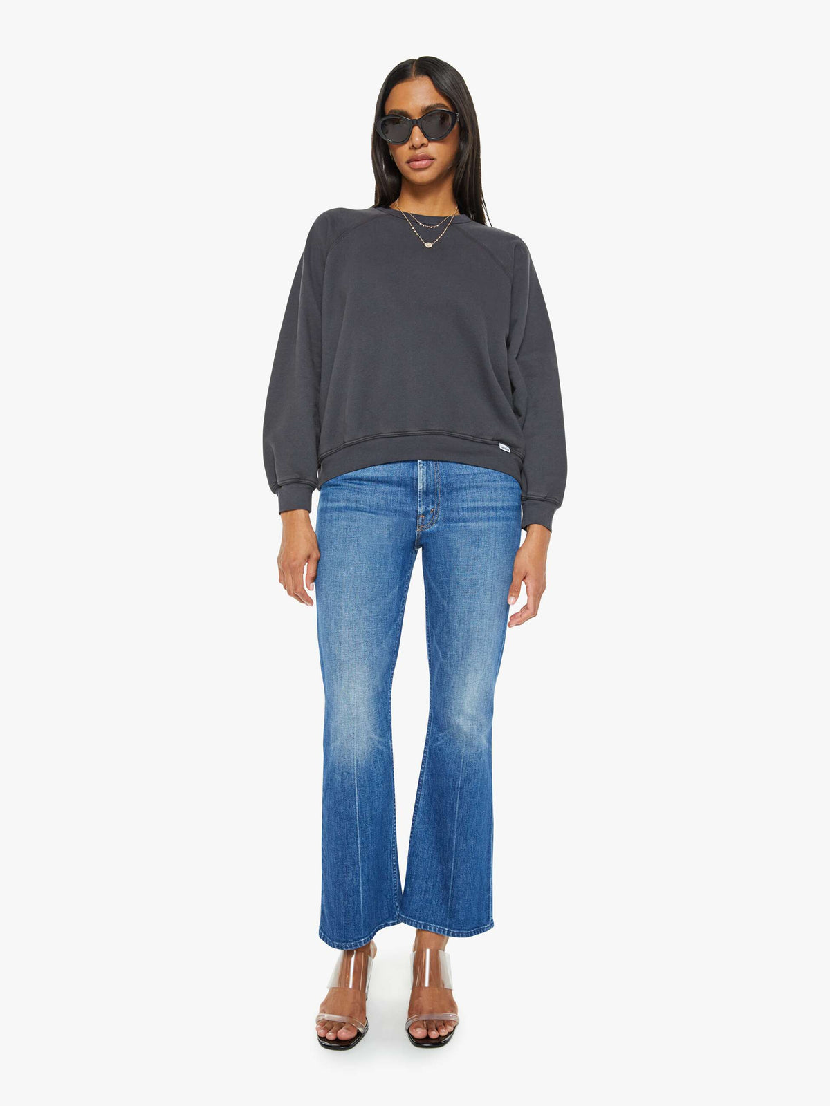 Woman wearing a dark gray sweatshirt and blue jeans on a white background
