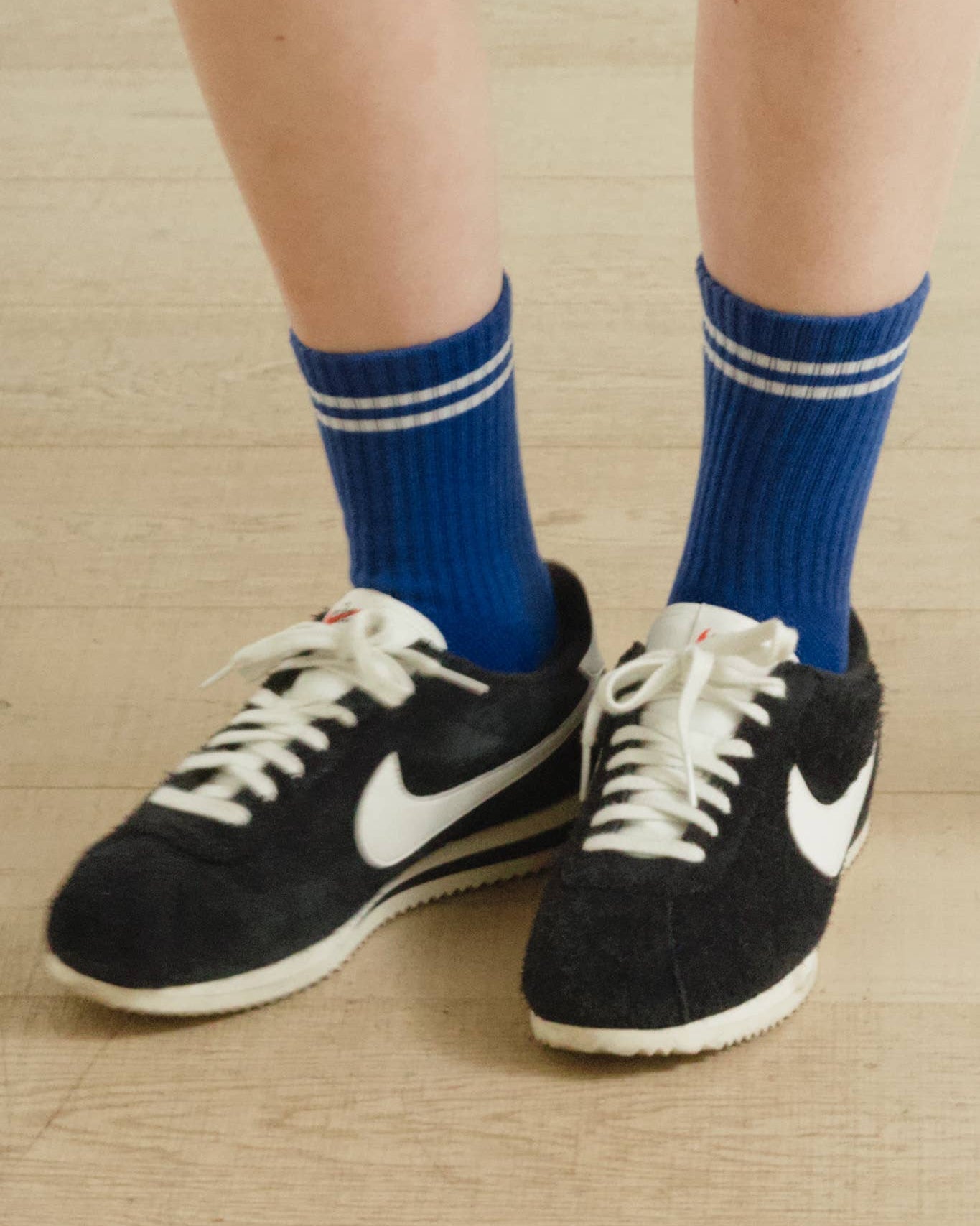 Black sneakers with white Nike logo worn with blue socks on a wooden floor.