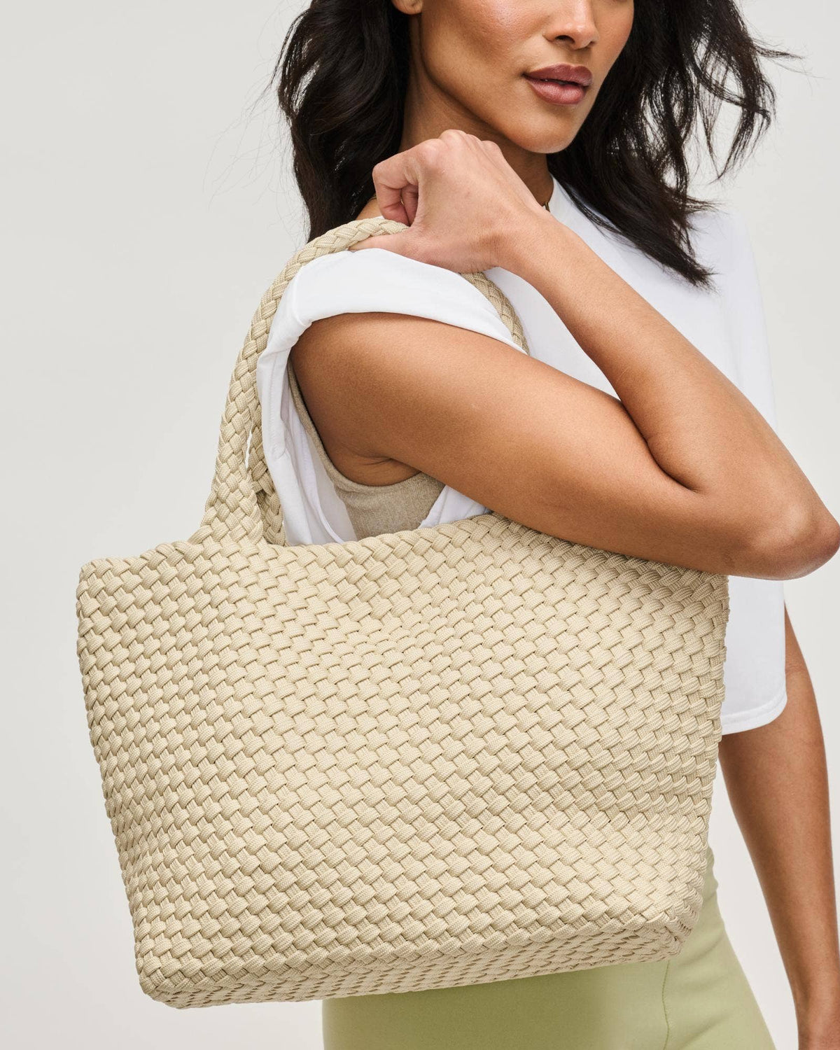 Woman holding a woven beige tote bag against a plain background