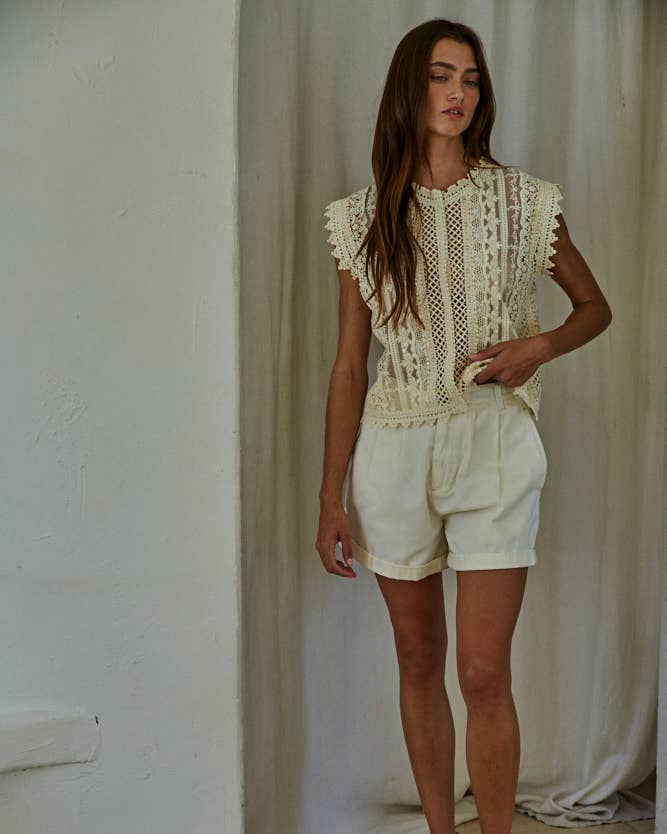 Woman wearing an off-white lace top and shorts in a minimal indoor setting