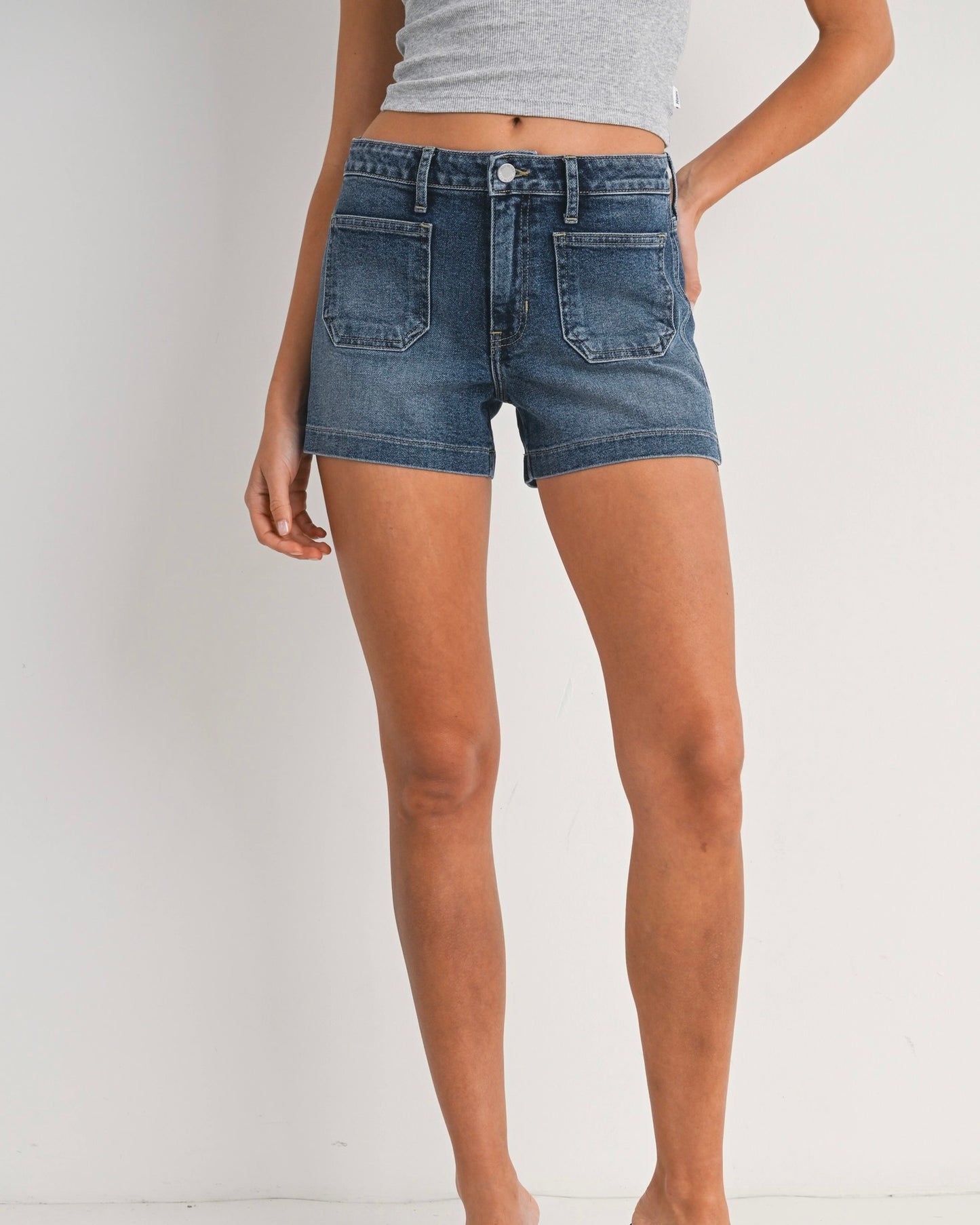 Front view of a model wearing the Just Black Denim patch pocket short standing in front of a white wall