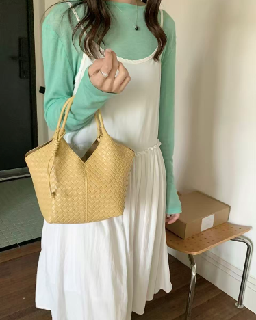 Person wearing a green long-sleeve top and white dress holding a yellow woven handbag.
