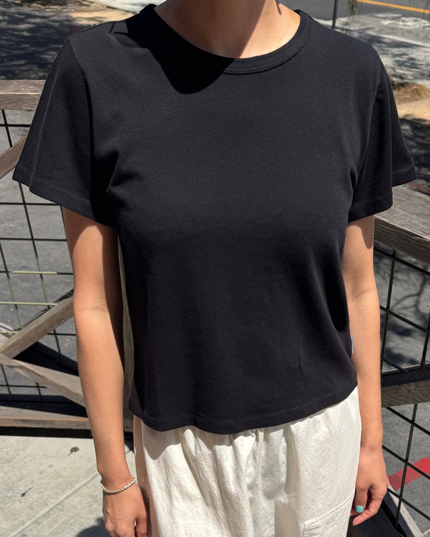 Person wearing a black t-shirt and white pants standing outdoors.