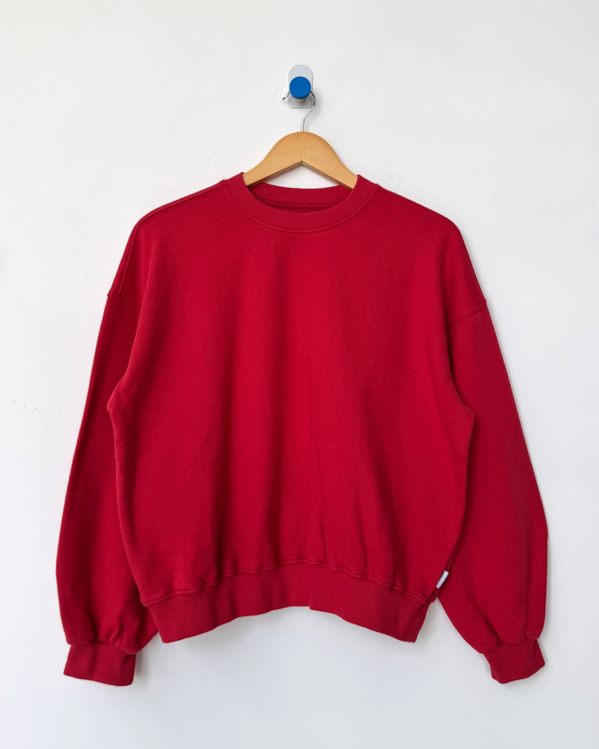 Red sweatshirt on a wooden hanger against a white background