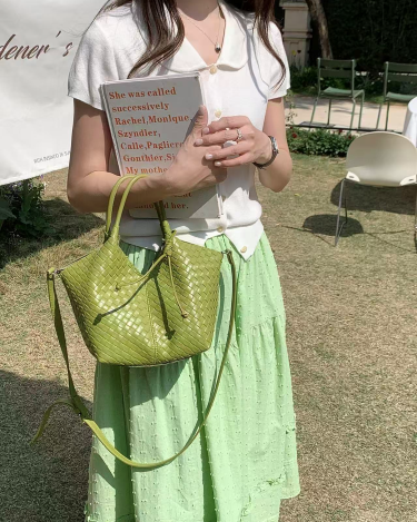 Person holding a book and a green handbag outdoors