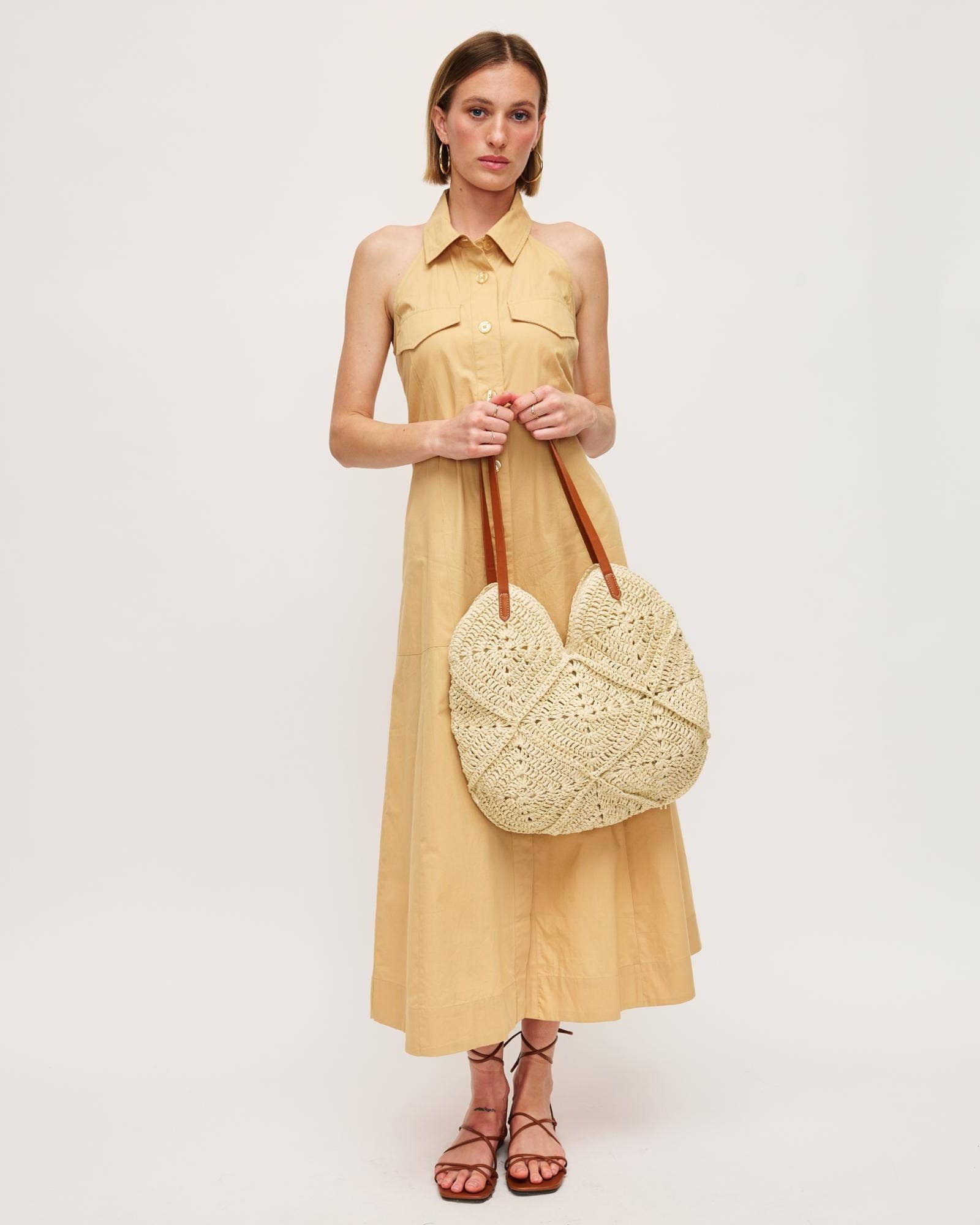 Woman in a yellow dress holding a woven bag on a white background