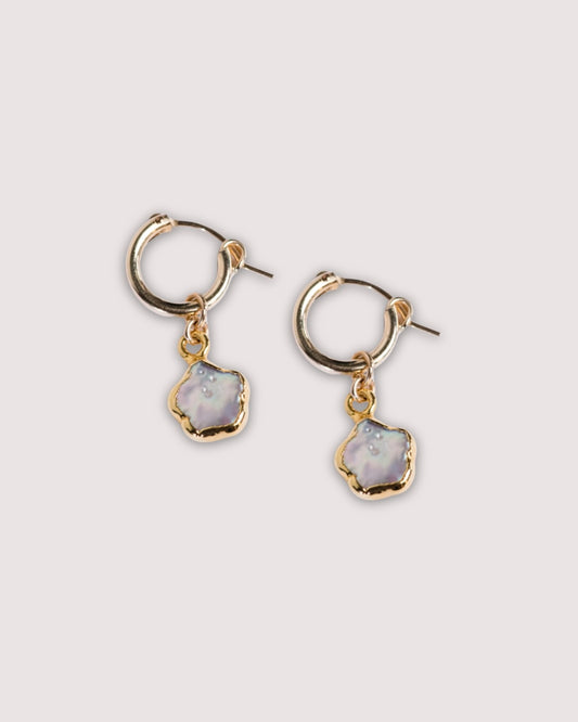 Close up photo of the Able Pearl Flower Huggie Hoops in gold laying against a solid white background.
