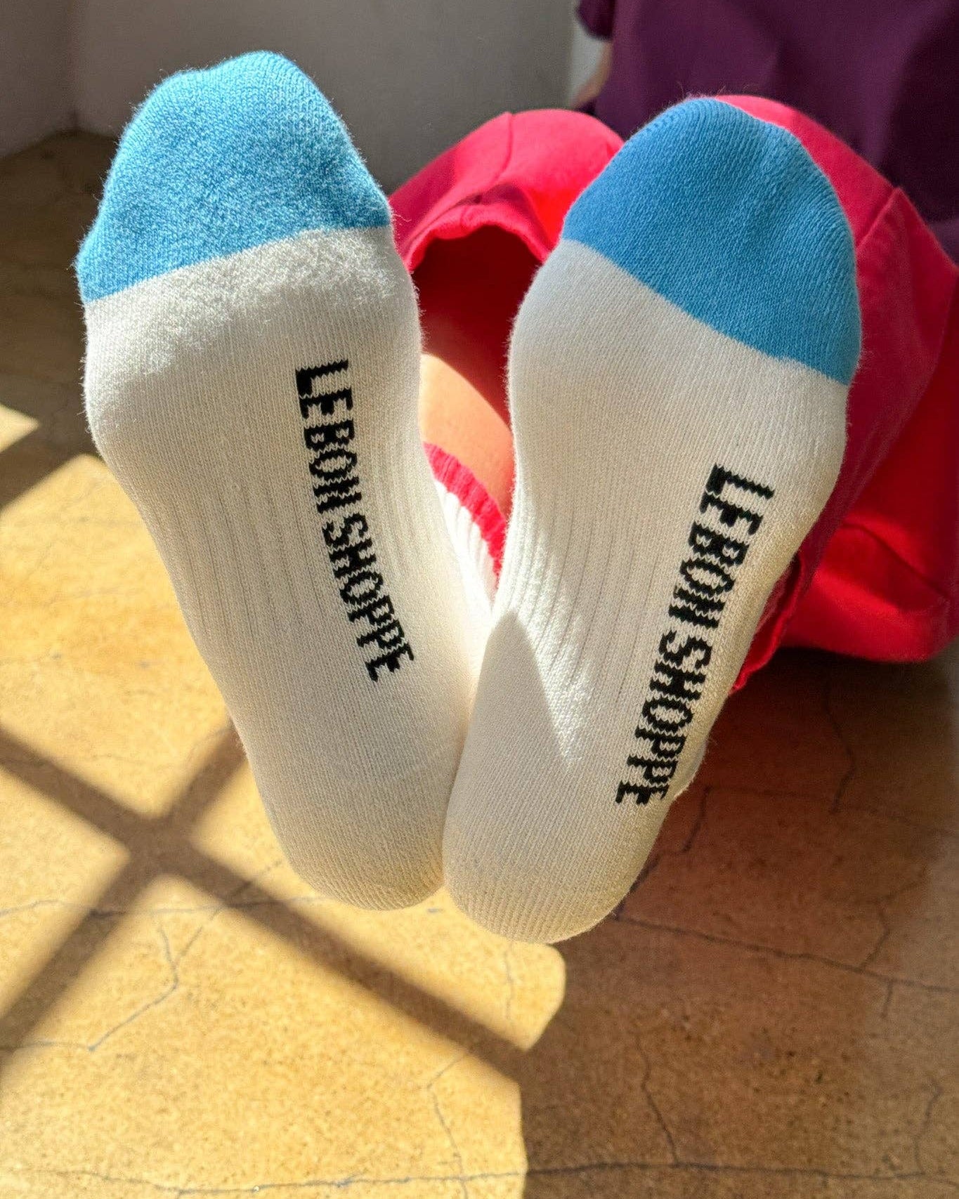 White socks with blue toes and 'LEBON SHOPPE' branding on a wooden floor.