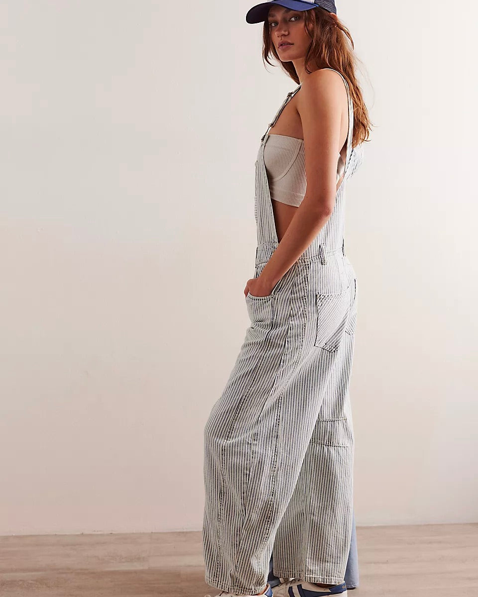 Side view of a model wearing the Free People Good Luck Stripe Overall standing in front of a white wall.