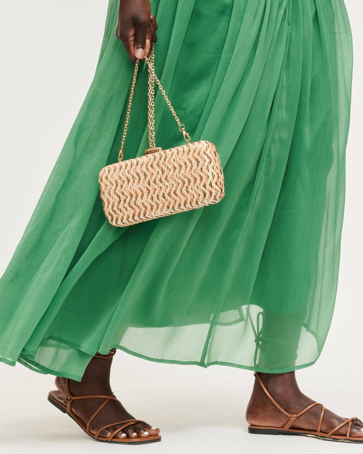 Person wearing a green dress holding a woven handbag on a white background