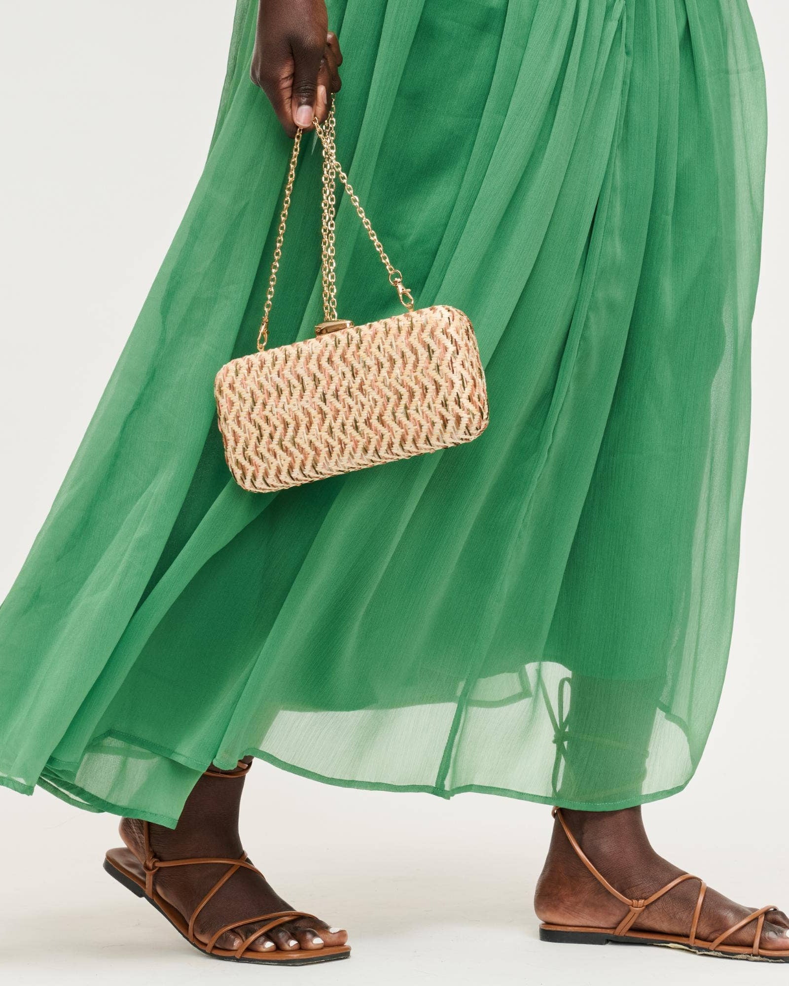 Person wearing a green dress holding a woven handbag on a white background