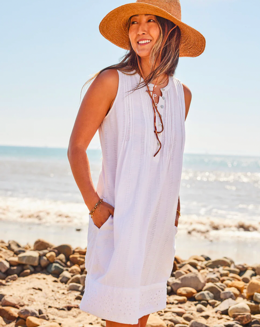 Model wearing Faherty Isha Eyelet Dress in white wearing a straw hat at the beach 