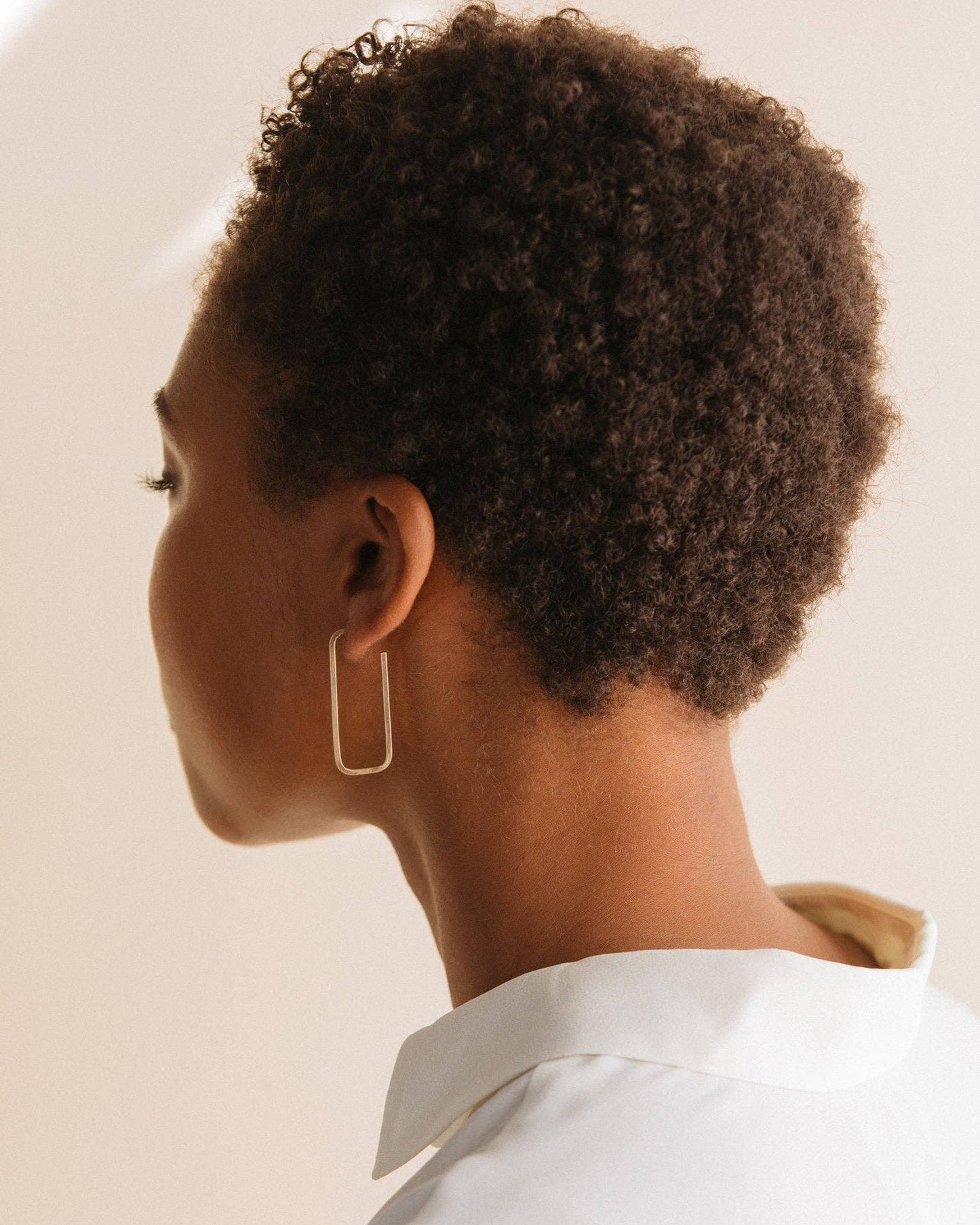 Person with short, curly hair wearing a gold earring against a neutral background