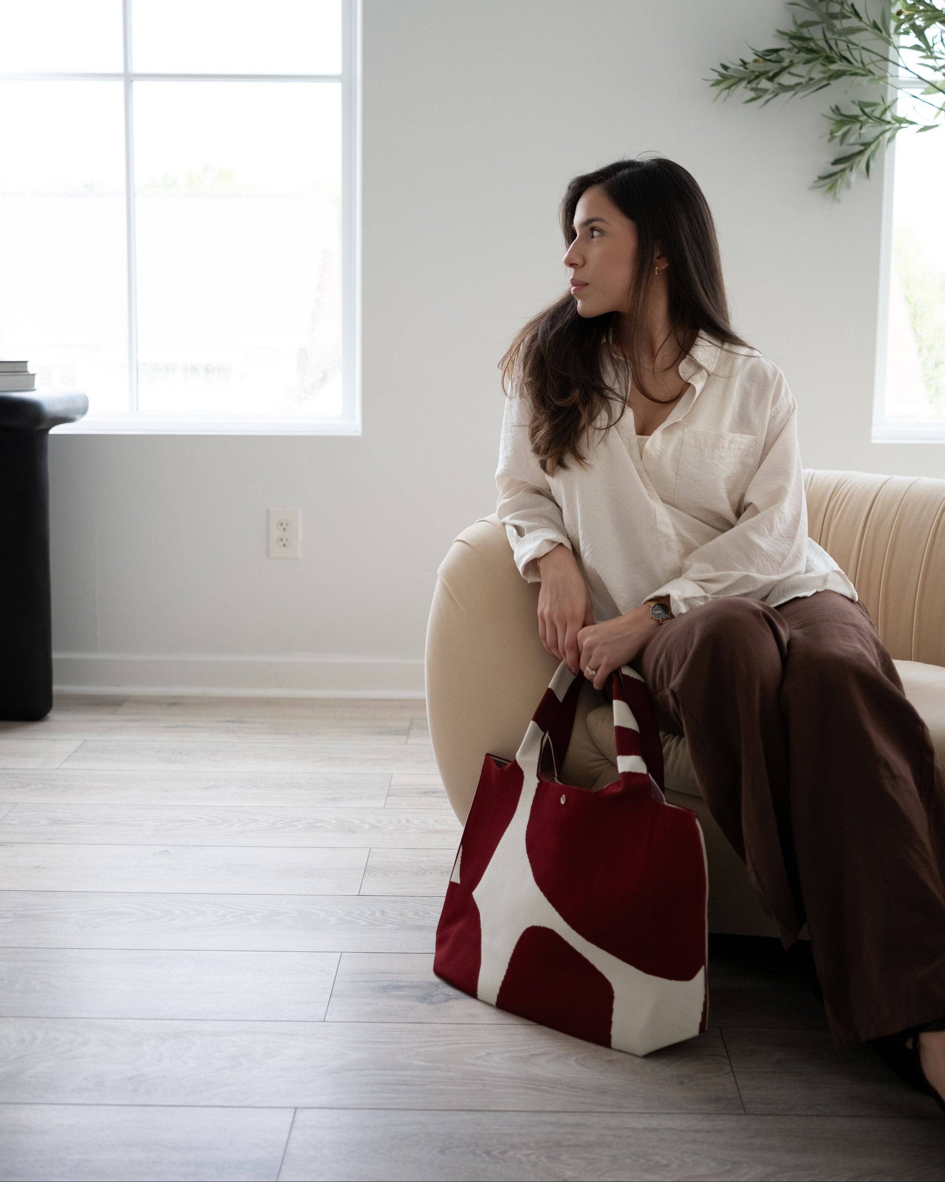 Woman sitting on a couch holding a red and white bag in a bright room.