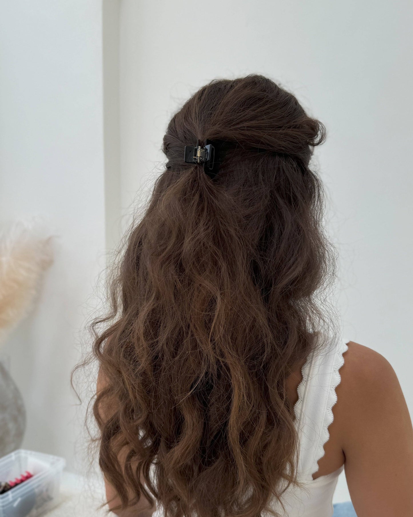 Person with long, wavy hair styled in a half-up, half-down style with a hair clip, against a neutral background.