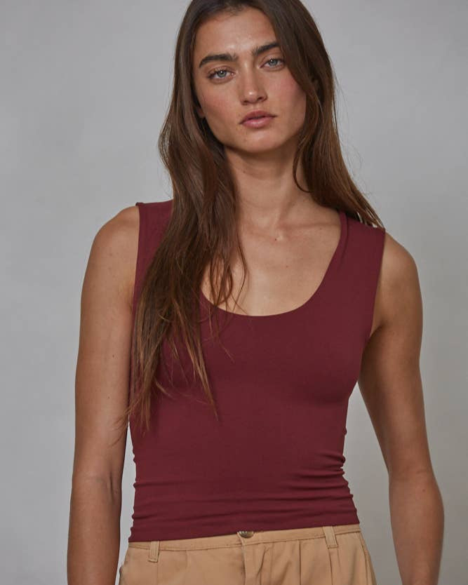 Woman wearing a maroon tank top and beige pants against a gray background