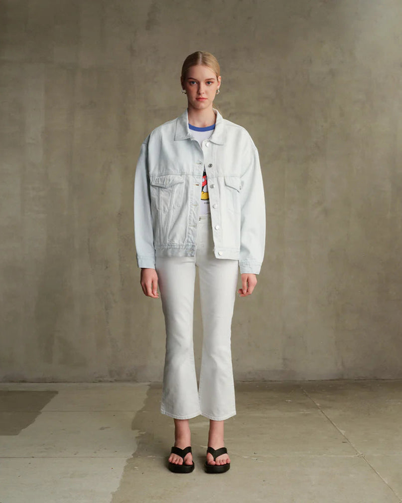 Person wearing a light denim jacket and white pants against a plain background