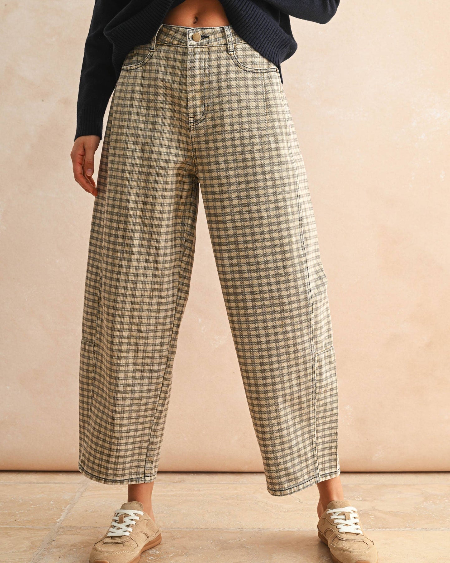 Person wearing plaid pants and a dark sweater against a beige background