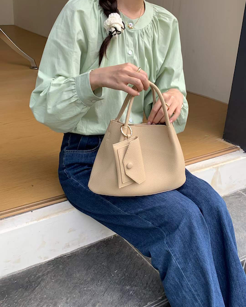 Person holding a beige handbag sitting on steps indoors