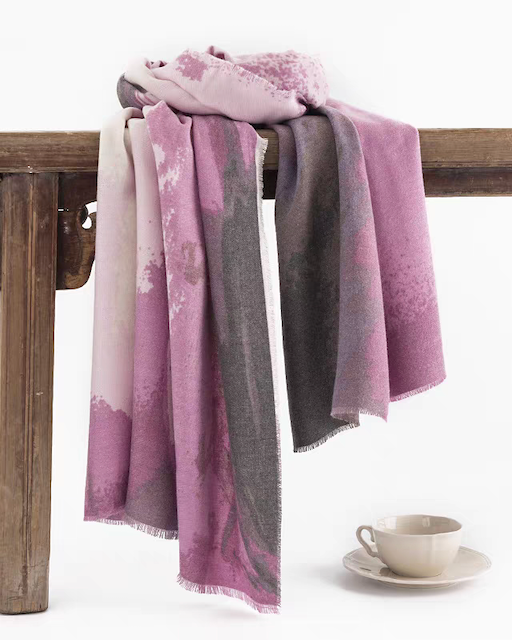 Purple and gray patterned scarf draped over a wooden table with a cup and saucer.