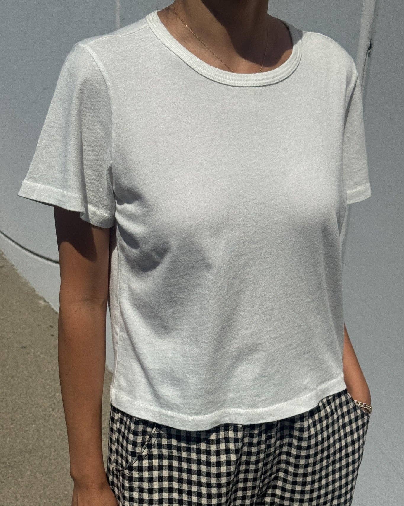 Person wearing a plain white t-shirt and checkered pants against a gray background