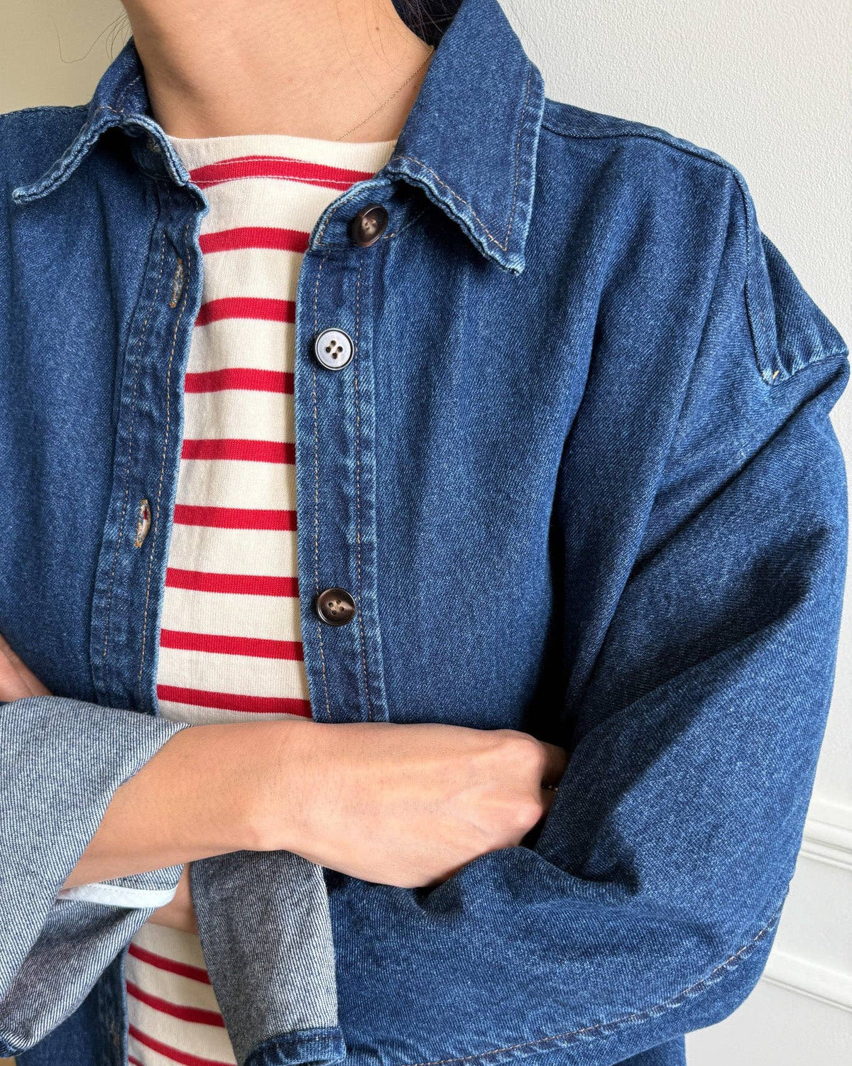 Person wearing a blue denim jacket over a red and white striped shirt.