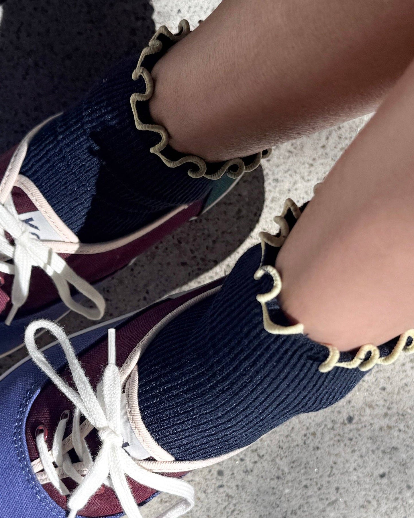 Close-up of maroon and blue sneakers with white laces on a concrete surface.