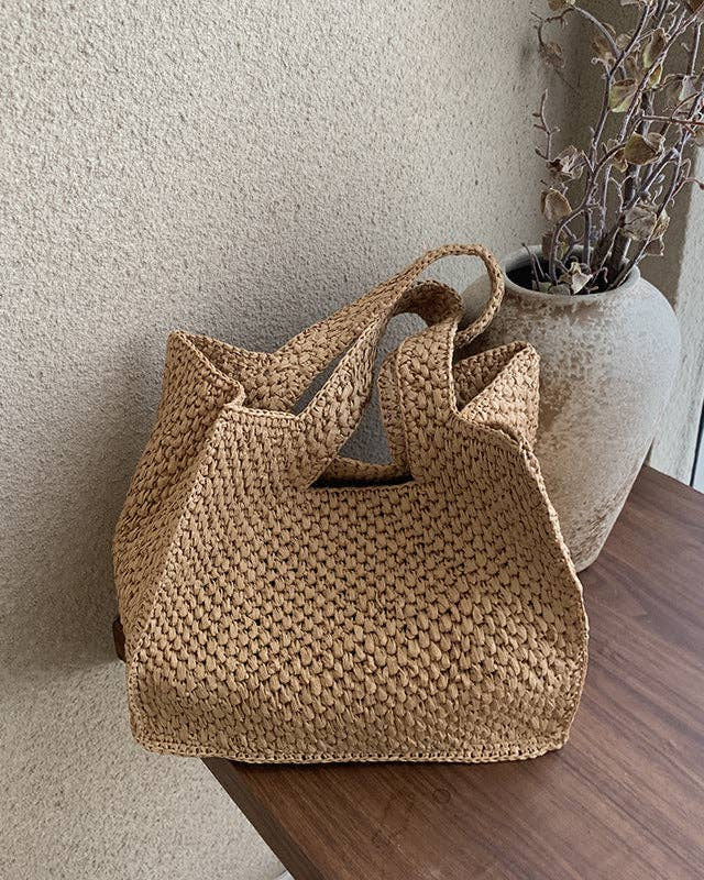 Woven brown handbag on a wooden surface with a neutral wall background