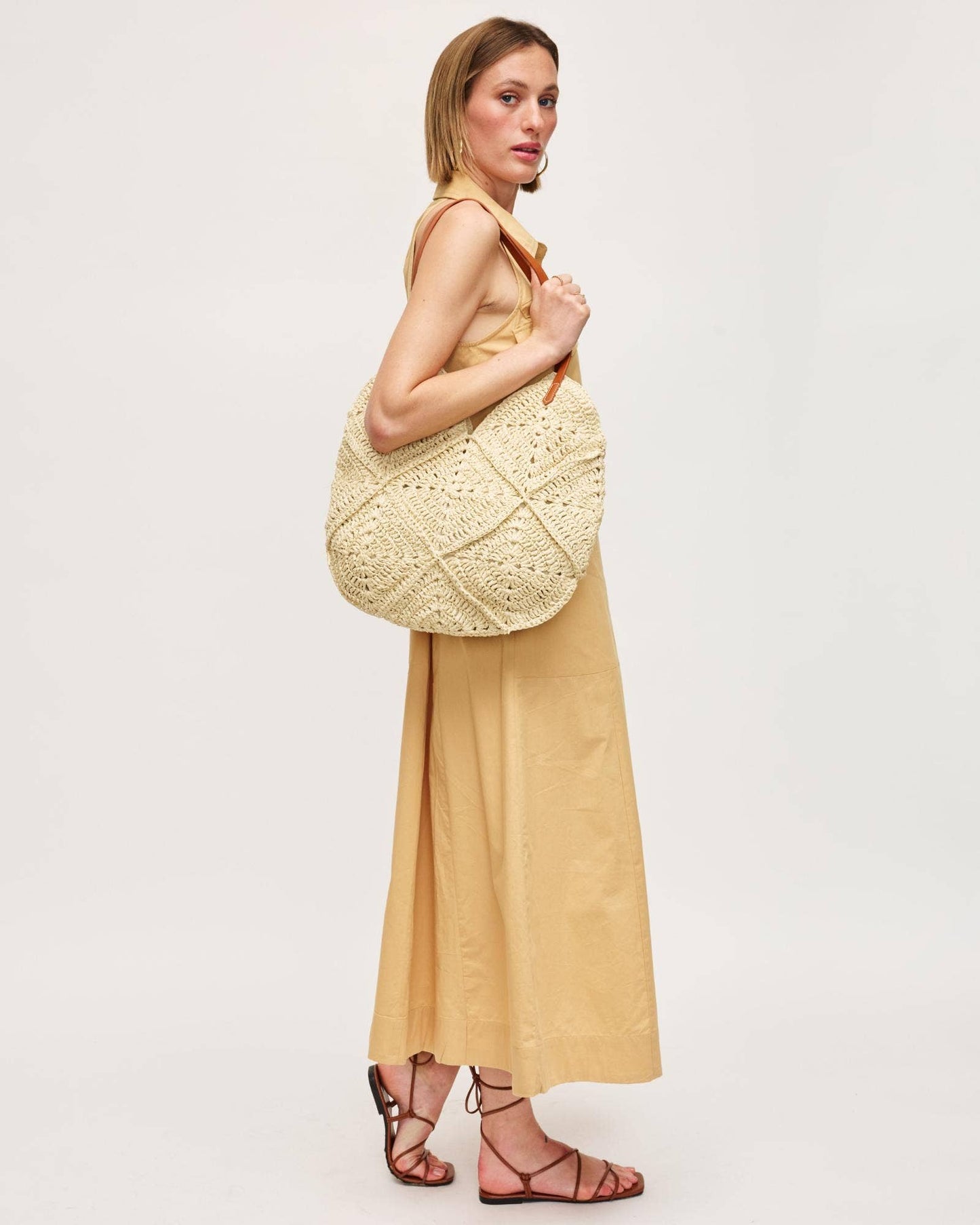 Woman holding a large woven beige bag against a plain background