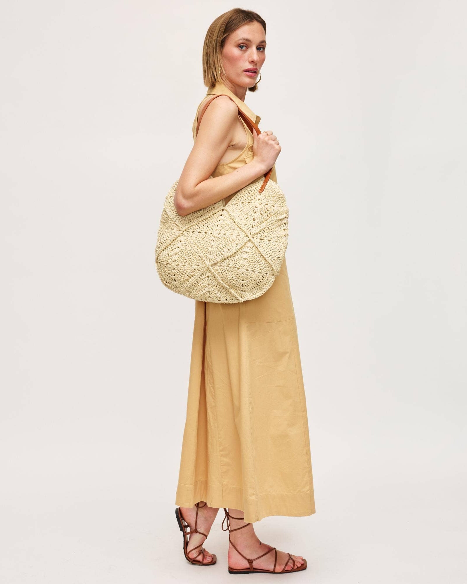 Woman holding a large woven beige bag against a plain background